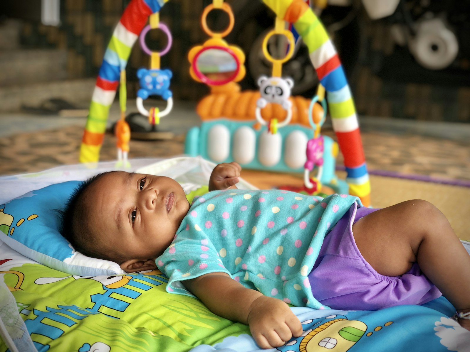 Bebé deitado num tapete de atividades com arco de brinquedos