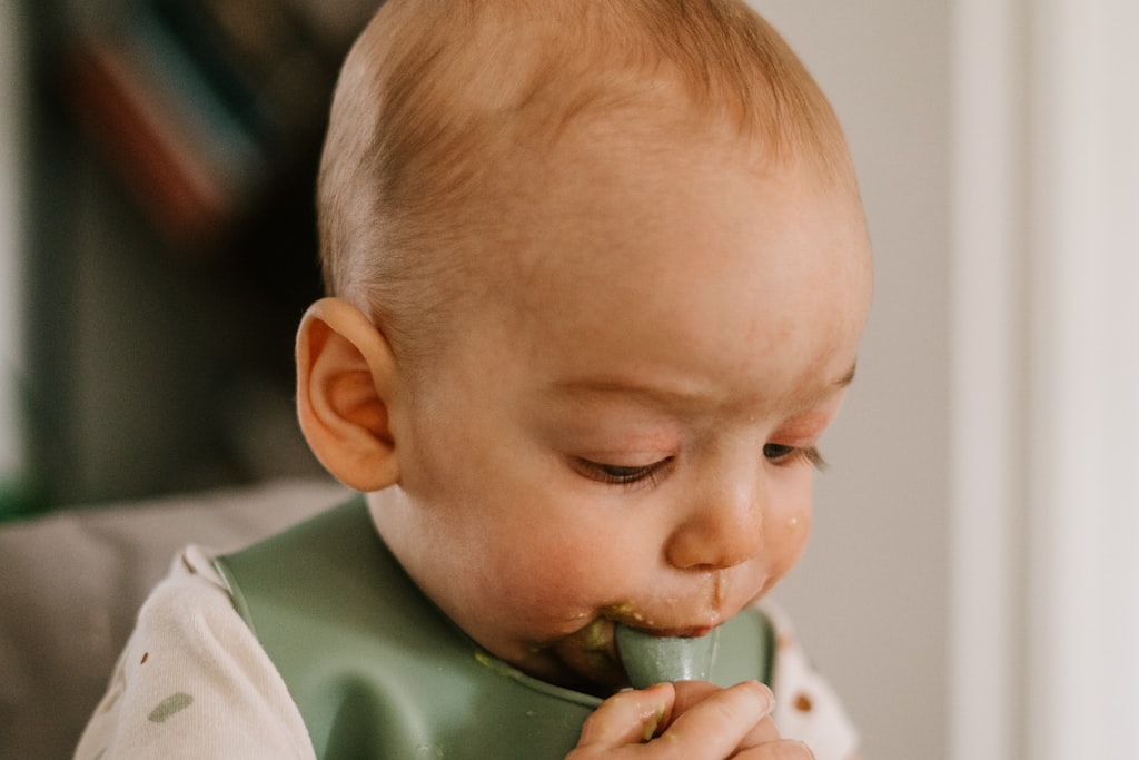 Bebé a comer sozinho com uma colher, com babete de silicone